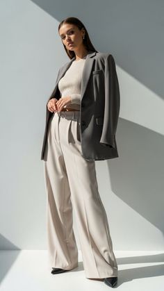 Woman in a blazer and wide leg pants against a white wall with shadows