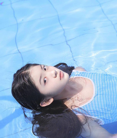 Woman with long black hair floating in a swimming pool wearing a blue dress