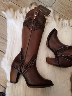 Pair of brown leather cowboy boots with embroidered details and studded accents on a white fur rug