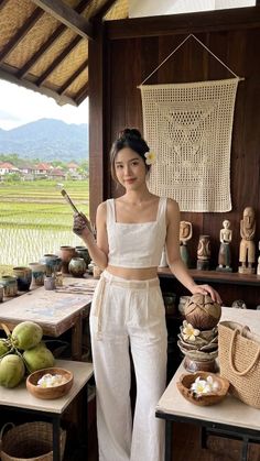 Woman in white outfit holding a paintbrush in an outdoor art studio overlooking rice paddies