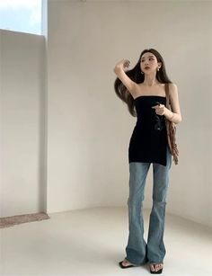 Woman in a black strapless top and flared jeans posing indoors