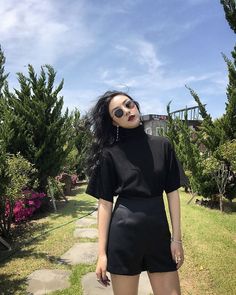 Woman in black top and shorts with sunglasses in a garden on a sunny day