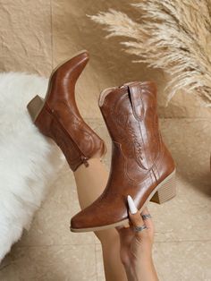 Brown cowboy boots with embroidery on a white fur rug with pampas grass