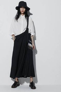 Woman in a black bucket hat, white shirt, and black pleated skirt in a studio