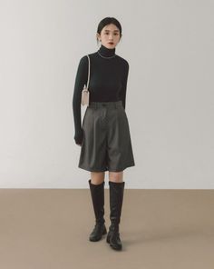 Woman in a black turtleneck, gray shorts, and knee-high boots in a studio