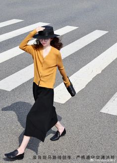 Woman in a yellow cardigan and black hat walking on a crosswalk