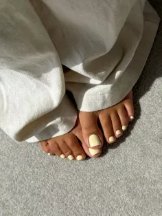 Feet with yellow nail polish on a gray carpet, wearing white pants