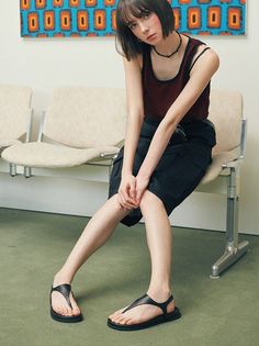 Woman with short hair wearing a striped tank top and black skirt, sitting indoors