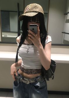 Woman in a leopard print hat and low rise jeans taking a mirror selfie