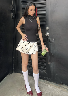 Woman in a black top and polka dot skirt holding a green drink outdoors