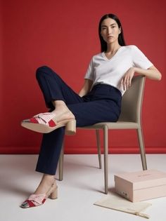 Woman in a white t-shirt and navy pants sitting on a chair against a red background