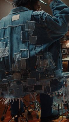 Person wearing a patchwork denim jacket from behind, holding drumsticks