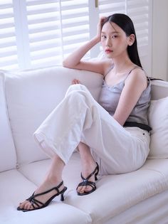 Woman with long black hair wearing a gray tank top and white pants on a white couch
