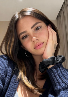 Woman with long dark hair and a blue sweater, wearing hoop earrings and a scrunchie