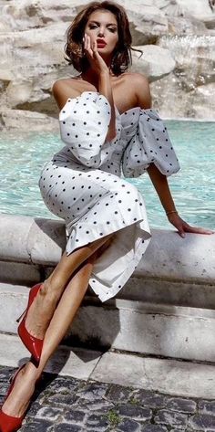 Woman in a polka dot dress and red heels posing by a water feature