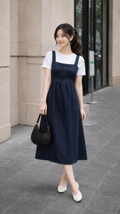 Woman in a denim dress and white t-shirt holding a black handbag outdoors