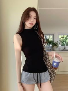 Woman with long hair in a black top and grey shorts holding a drink indoors