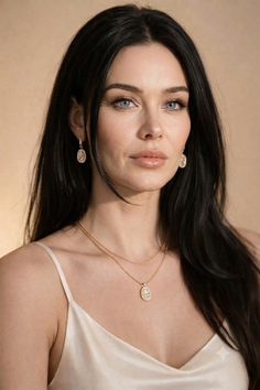Woman with long black hair and blue eyes wearing a slip dress and gold jewelry