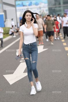Woman with long dark hair wearing a white t-shirt and ripped jeans walking on a street