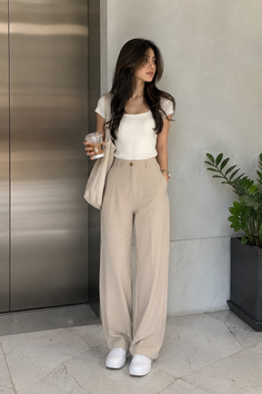 Woman in a white top and wide leg pants holding a drink indoors