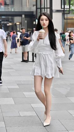 Woman in a white dress with long black hair walking on a street