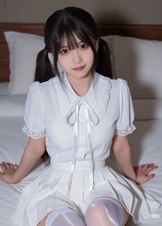 Woman in a white shirt and pleated skirt with thigh-high socks sitting on a bed