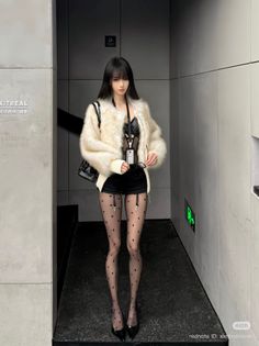 Woman in a fur jacket, black shorts, and polka dot stockings indoors