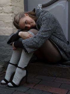 Woman in a plaid coat and grey socks sitting on outdoor steps