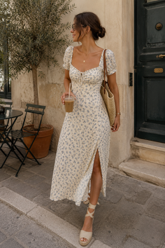 Woman in a floral dress and espadrille sandals holding iced coffee on a street