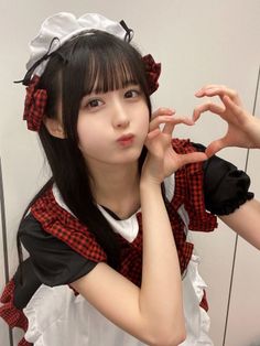 Woman in a maid outfit with red plaid details making a heart shape with her hands
