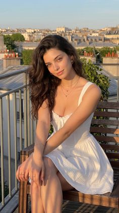 Woman in a white dress sitting on a rooftop at golden hour with a cityscape background