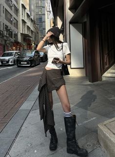 Woman in a plaid skirt, beanie, and knee-high boots on a city street