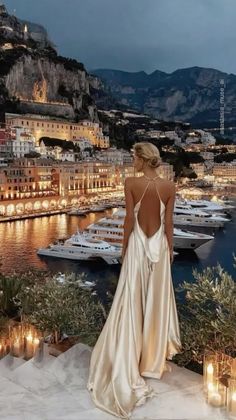 Woman in a backless dress overlooking a lit-up harbor at night