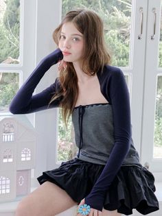 Young woman in a striped top and mini skirt sitting by a window with a dollhouse