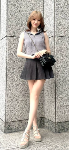 Woman with light brown hair in a pleated skirt and sleeveless top posing outdoors