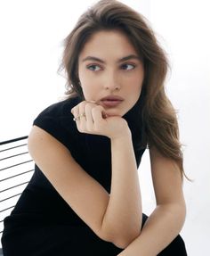 Woman with long brown hair wearing a black turtleneck dress and rings