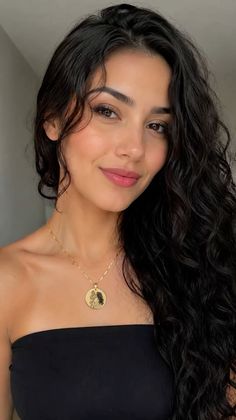 Woman with long curly black hair wearing a strapless top and gold necklace