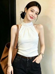 Woman in a white halter top and black jeans with a brown shoulder bag