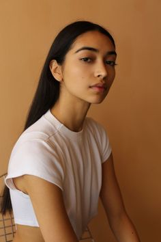 Woman with long dark hair wearing a white t-shirt against a brown background