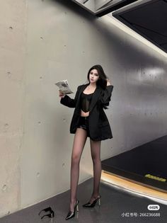 Woman in a black blazer, sheer top, and leather shorts holding a newspaper
