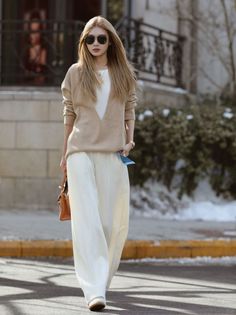 Woman with long hair and sunglasses wearing a sweater and wide leg pants outdoors