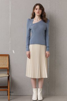 Woman in a blue sweater and pleated skirt standing indoors