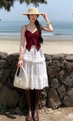 Woman in a straw hat and red top with a white skirt and brown boots on a beach