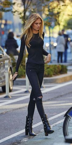 Woman with long blonde hair walking on a street in black top and ripped jeans