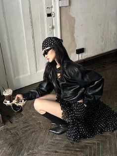 Woman in a leather jacket and polka dot skirt holding drinks, crouching indoors