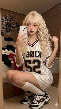 Woman with long blonde curly hair taking a mirror selfie in an oversized jersey