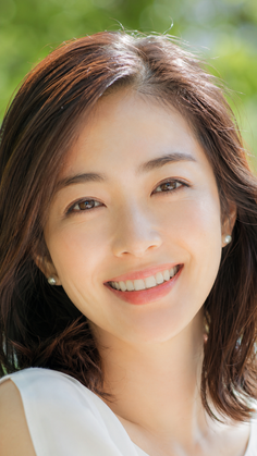 Woman with short brown hair and pearl earrings smiling outdoors