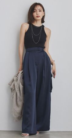 Woman in a black tank top and wide leg pants holding a scarf