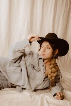Woman in a denim shirt and cowboy hat with a long braid, lying down indoors