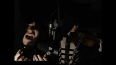 Two people in dark clothing, one screaming into a microphone, the other playing a violin